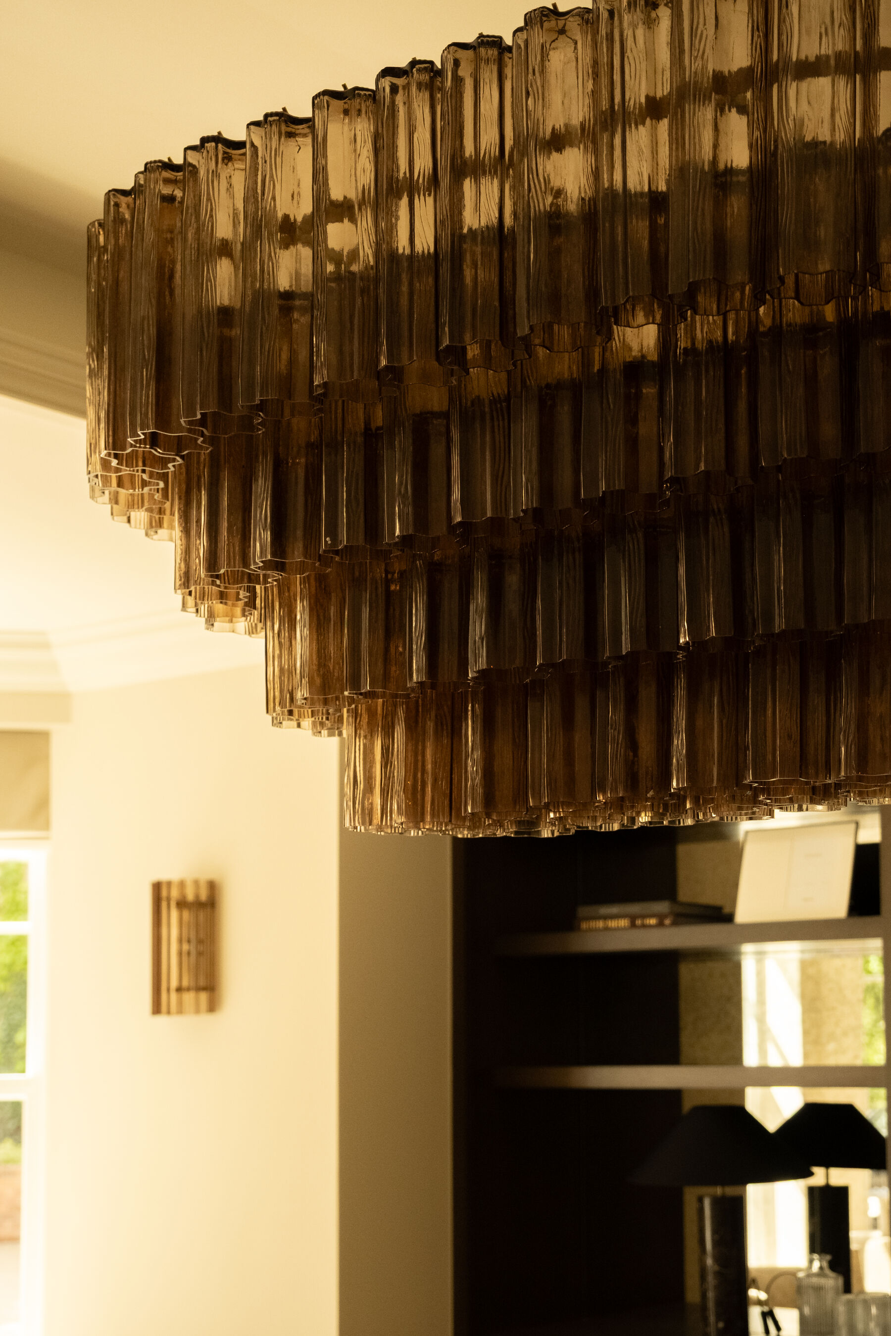 Tiered smoked glass chandelier against a soft plaster wall