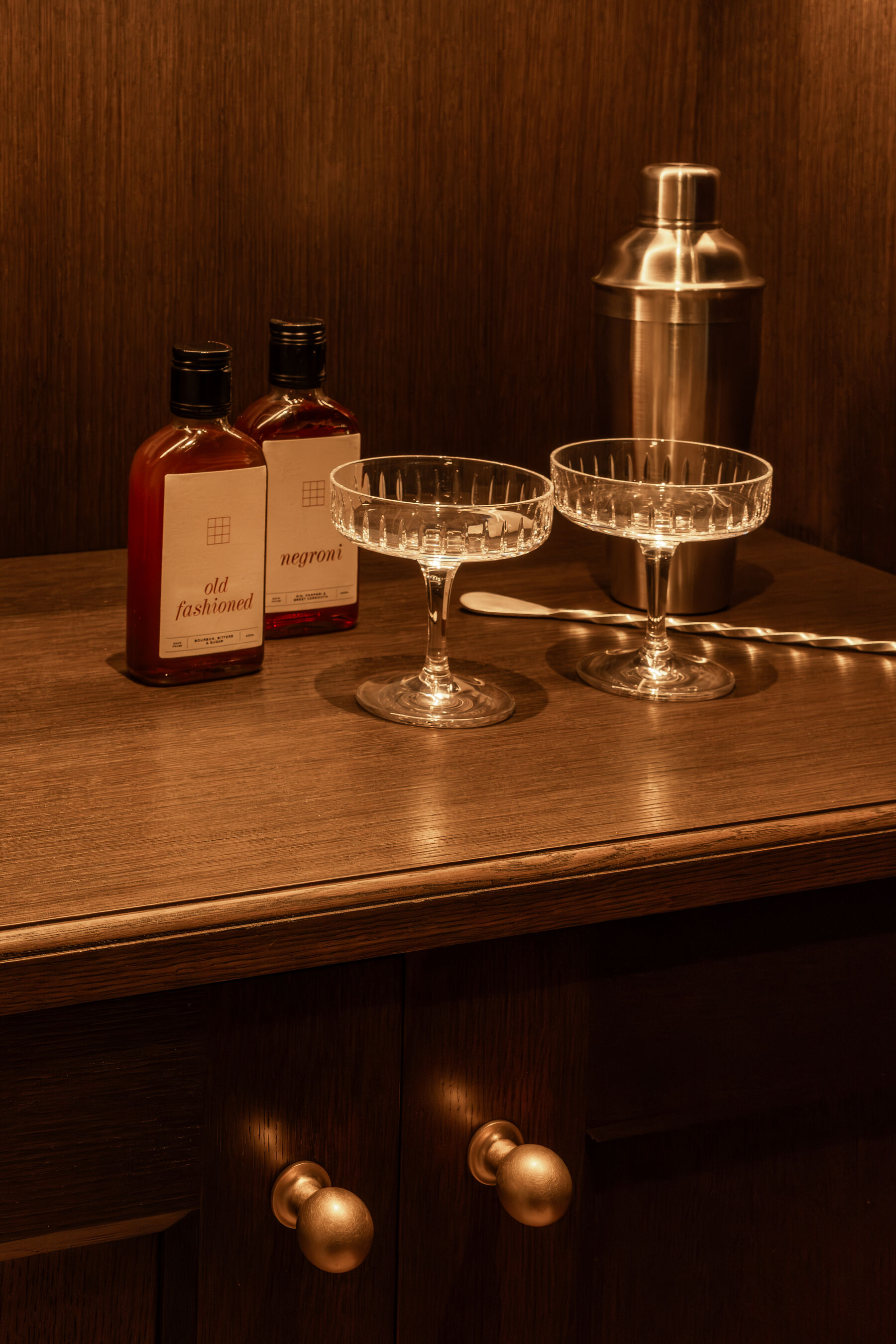 Cut crystal coupes, shaker and bitters on a fumed oak bar top