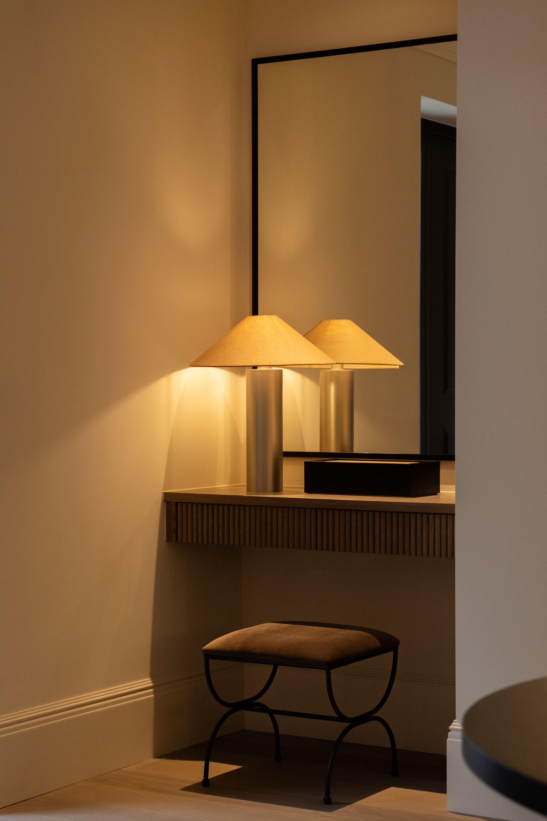 Fluted console with paired brass lamps beneath a framed mirror